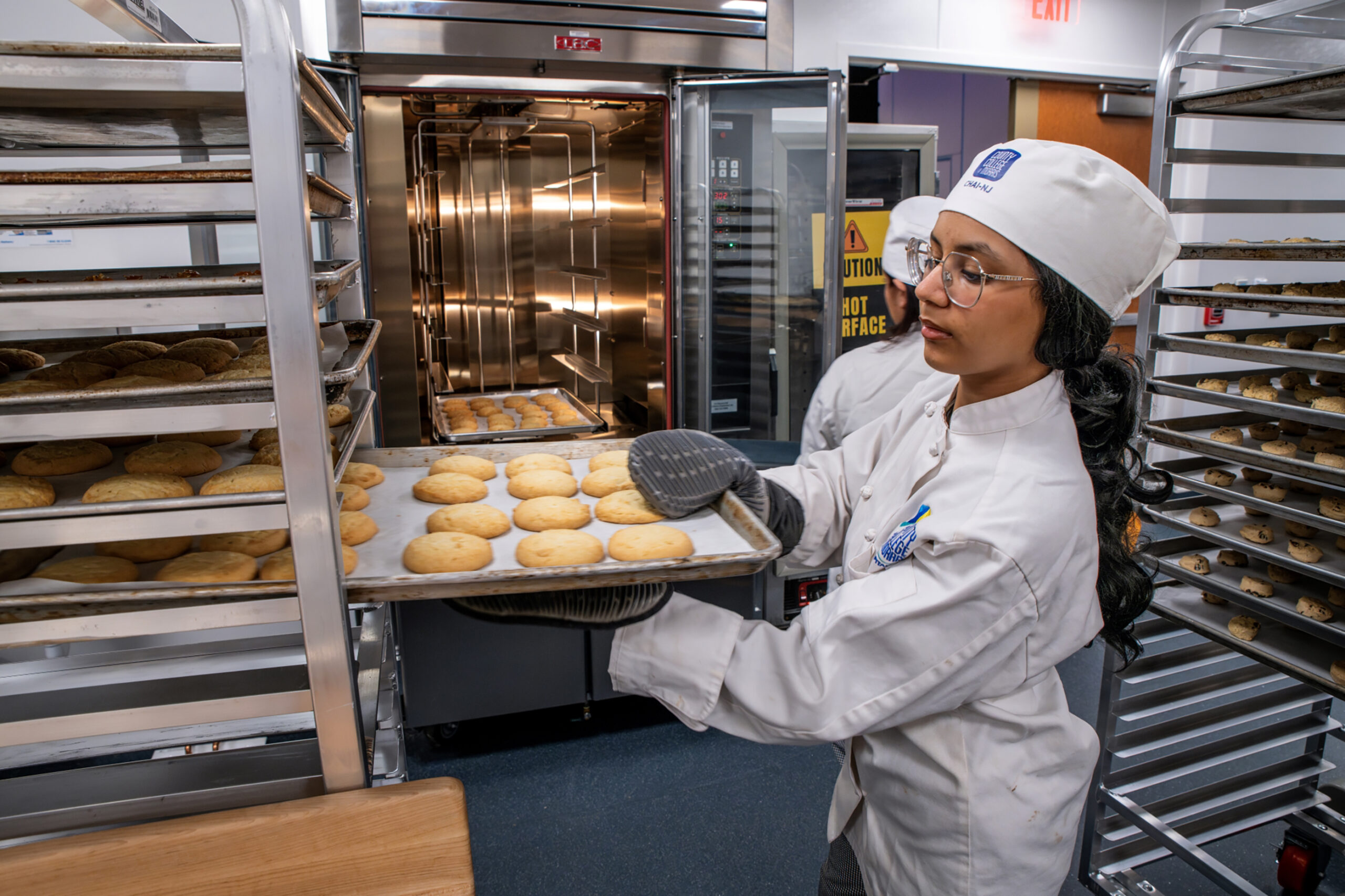 Female Student placing cookies onto tall rack cooling rack