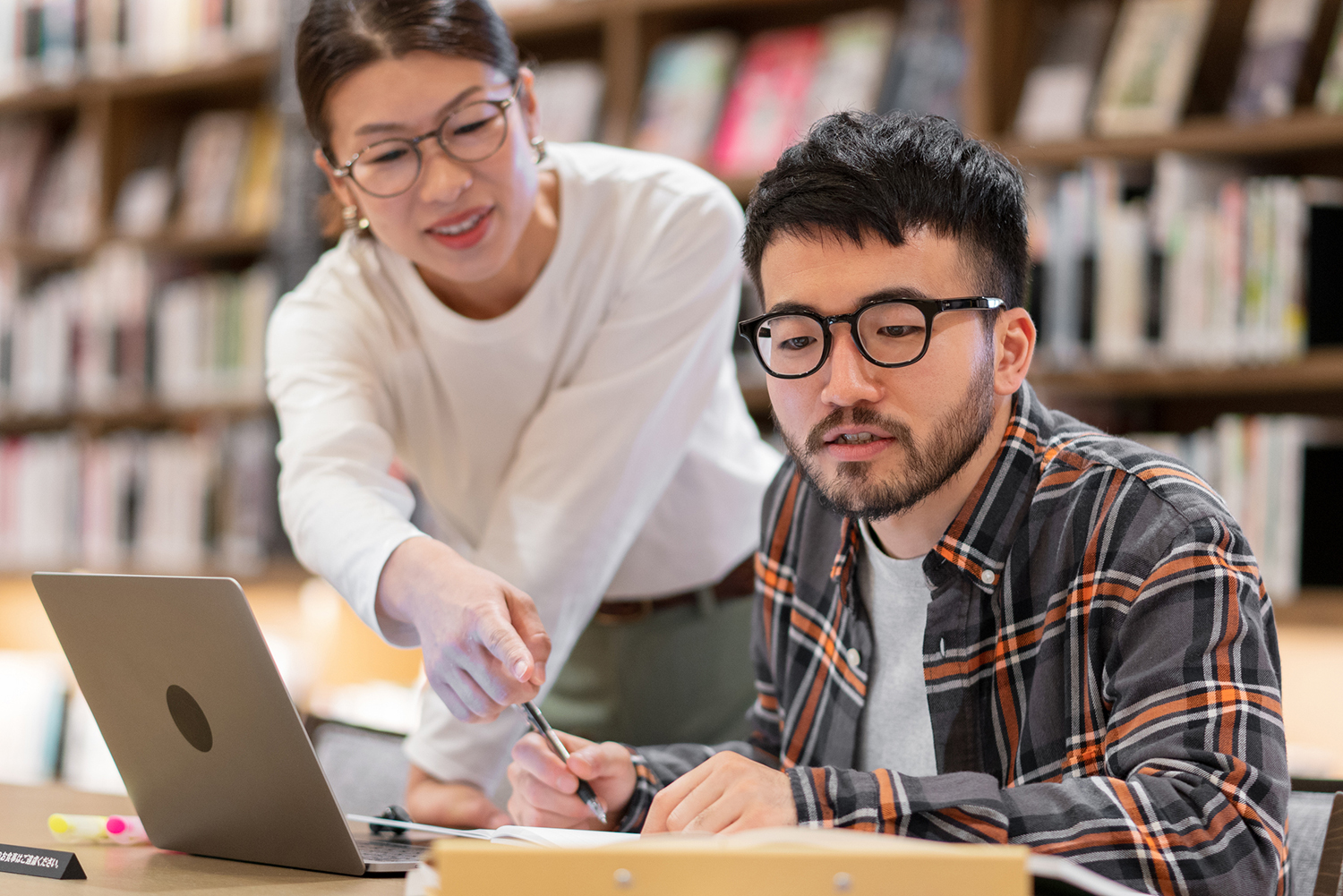 Image of women helping student on computer in library