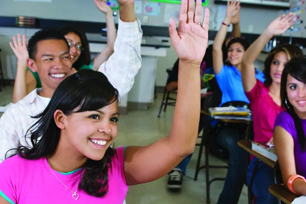 Image of a classroom of high school students with hispanic female raising her hand