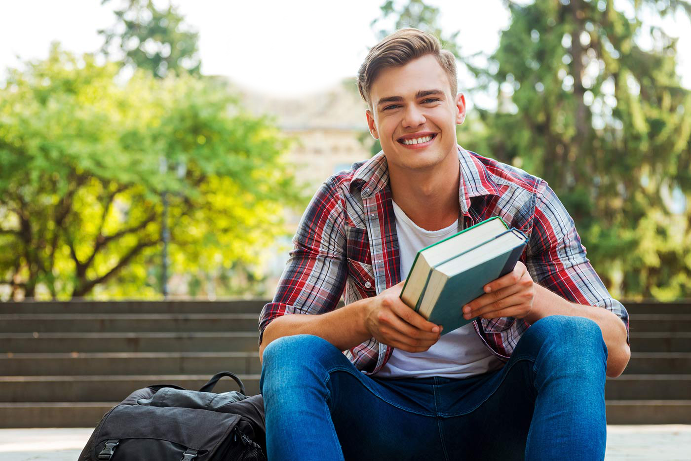 Image of student sitting on bench with books in his hand smiling at camera.