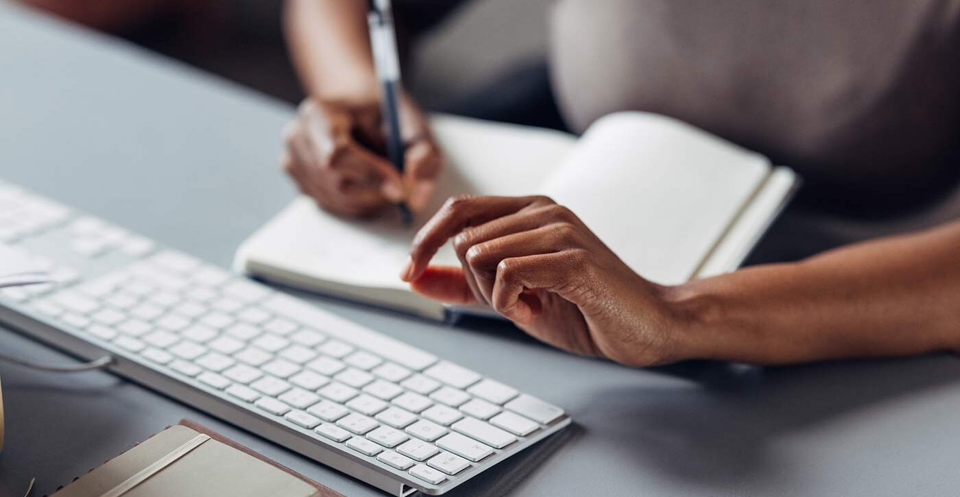 Woman writing in notebook by computer keyboard